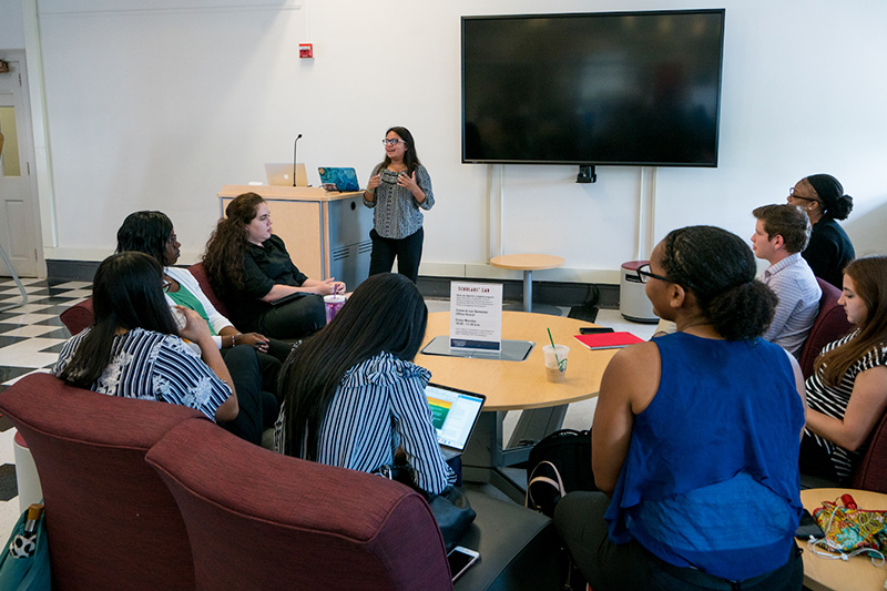 A group of students in comfy chairs with someone giving an informal presentation nearby.